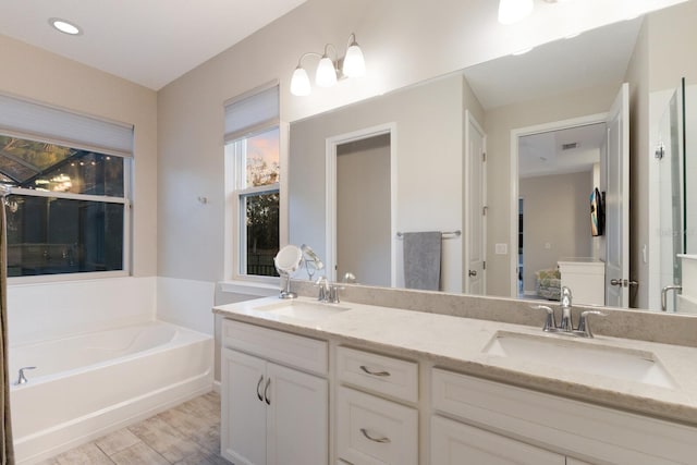 full bathroom featuring wood finished floors, double vanity, a sink, and a bath