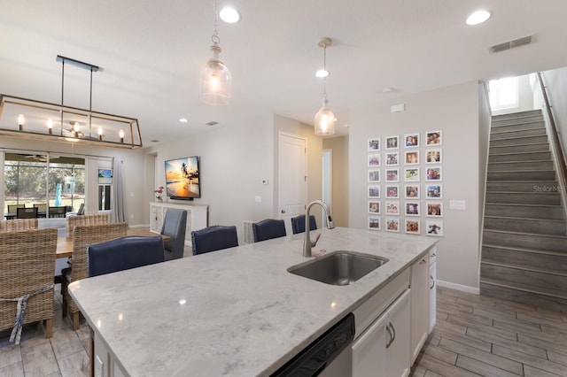 kitchen with a sink, visible vents, white cabinetry, light stone countertops, and a center island with sink