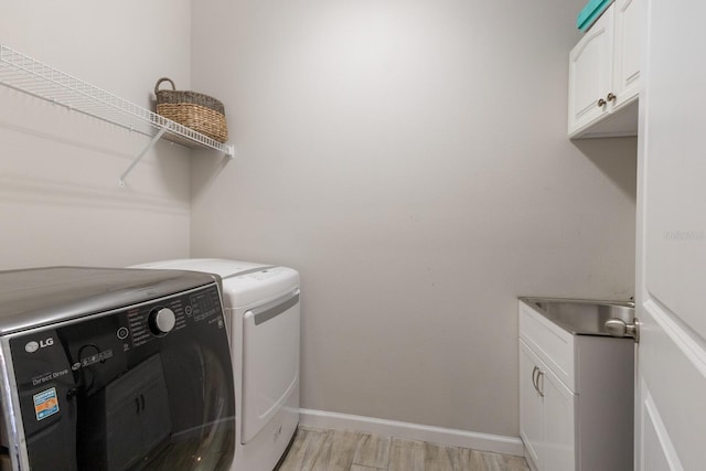 washroom with cabinet space, washing machine and dryer, baseboards, and light wood-style flooring