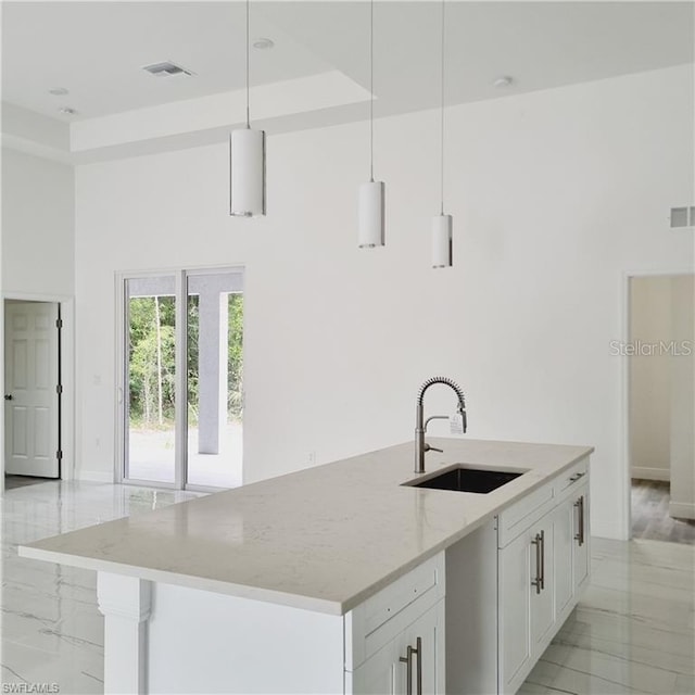 kitchen with white cabinets, light stone counters, decorative light fixtures, a kitchen island with sink, and a sink