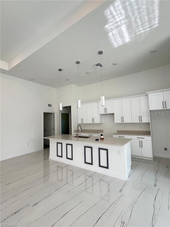 kitchen featuring a sink, white cabinets, light countertops, an island with sink, and decorative light fixtures