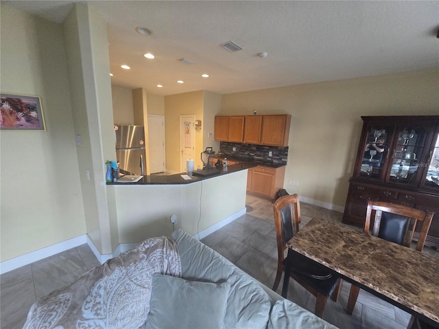 kitchen featuring visible vents, baseboards, freestanding refrigerator, tasteful backsplash, and dark countertops