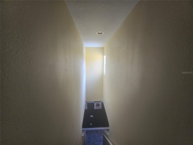 corridor featuring a textured ceiling and a textured wall