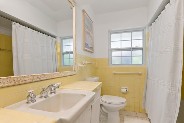 bathroom featuring tile patterned flooring, toilet, vanity, tile walls, and wainscoting