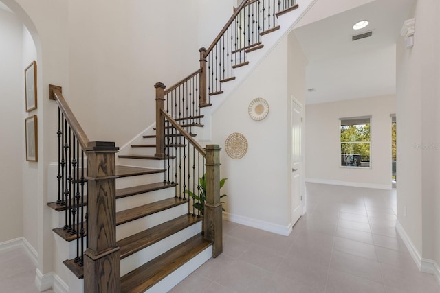 stairway featuring tile patterned flooring, a towering ceiling, visible vents, and baseboards