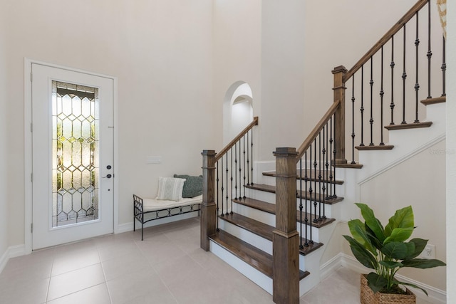 entryway featuring light tile patterned floors, stairs, a towering ceiling, and baseboards