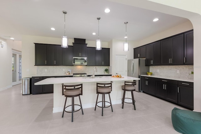 kitchen with a center island with sink, a breakfast bar area, stainless steel appliances, light countertops, and a sink