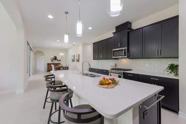 kitchen with tasteful backsplash, arched walkways, a kitchen island with sink, stainless steel appliances, and a sink