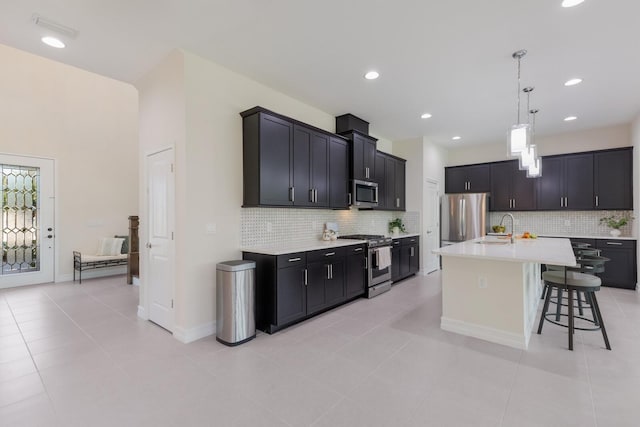 kitchen with light countertops, appliances with stainless steel finishes, a kitchen island with sink, a sink, and a kitchen breakfast bar