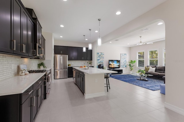 kitchen with arched walkways, appliances with stainless steel finishes, open floor plan, light countertops, and a sink