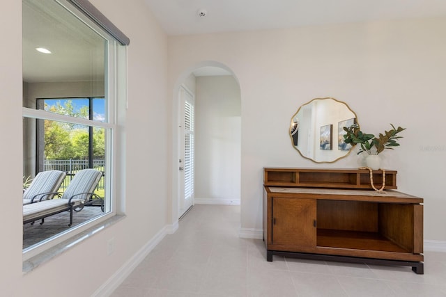 hall featuring light tile patterned floors, baseboards, and arched walkways