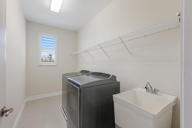 laundry area with light tile patterned flooring, washing machine and dryer, laundry area, a sink, and baseboards