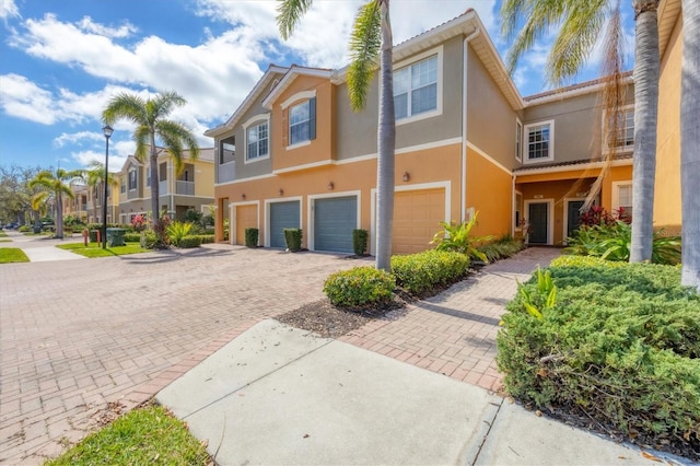 townhome / multi-family property with an attached garage, a residential view, decorative driveway, and stucco siding