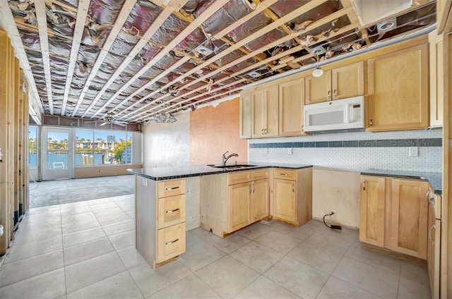 kitchen with light brown cabinets, a sink, a peninsula, and white microwave