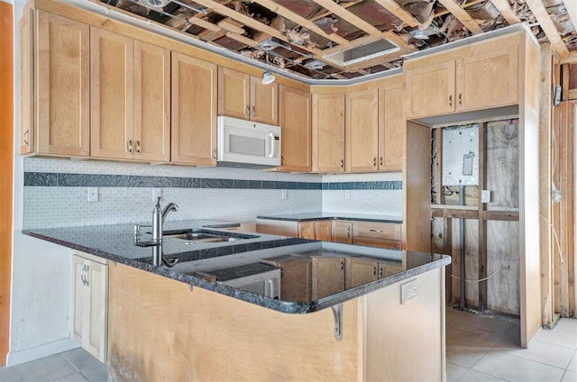 kitchen with white microwave, light tile patterned flooring, a sink, light brown cabinetry, and dark stone countertops