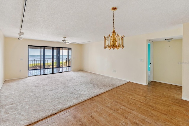 empty room with a textured ceiling, a water view, wood finished floors, carpet flooring, and baseboards