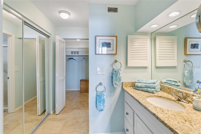 bathroom with visible vents, a spacious closet, vanity, a textured ceiling, and tile patterned floors