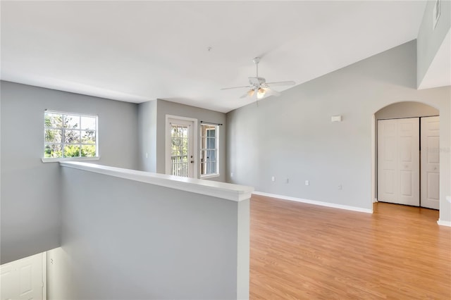 unfurnished room with a ceiling fan, light wood-type flooring, vaulted ceiling, and baseboards