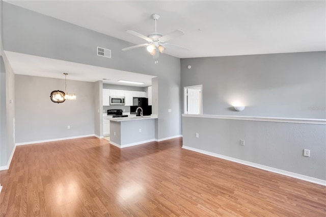 unfurnished living room featuring visible vents, light wood-style floors, vaulted ceiling, baseboards, and ceiling fan with notable chandelier