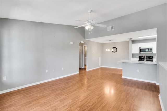 unfurnished living room featuring arched walkways, ceiling fan with notable chandelier, visible vents, baseboards, and light wood-type flooring