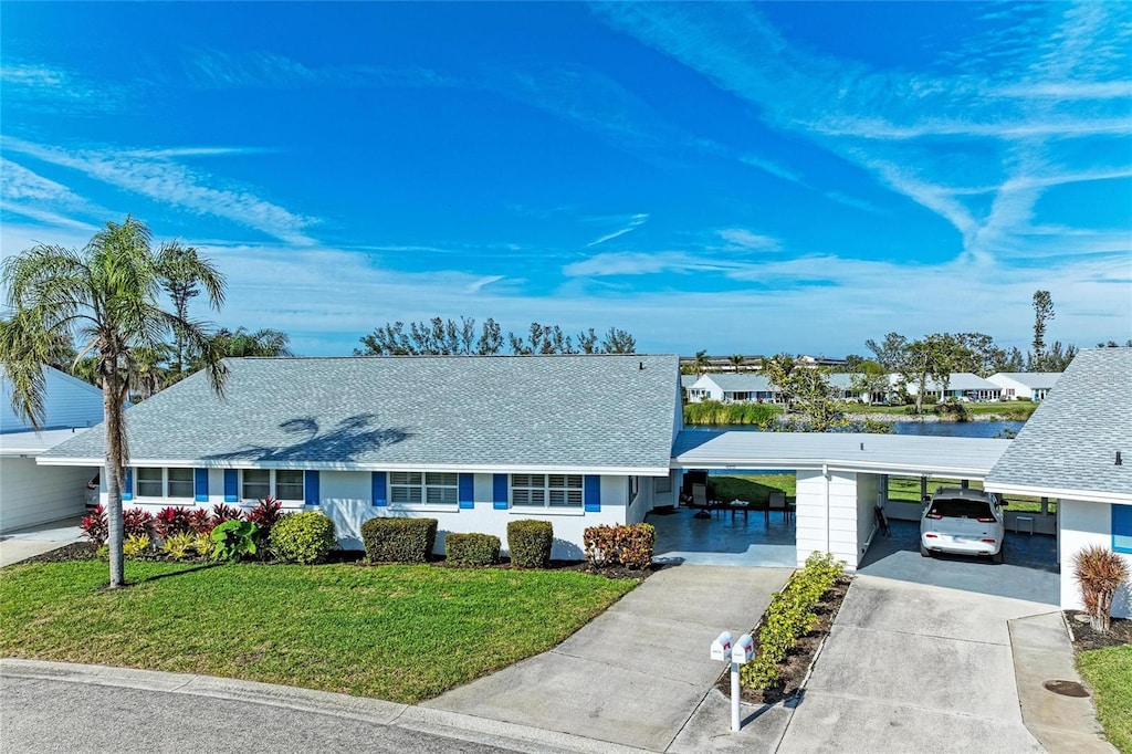 ranch-style house with a carport, a front yard, concrete driveway, and a shingled roof