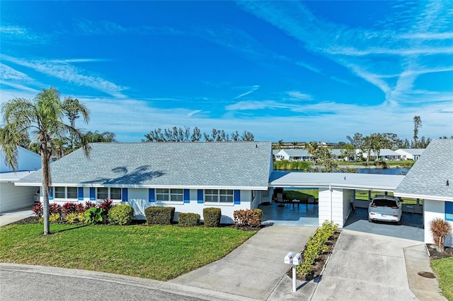 ranch-style house with a carport, a front yard, concrete driveway, and a shingled roof