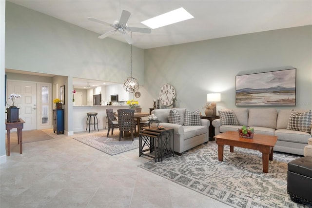 living area featuring a ceiling fan, a skylight, a towering ceiling, and baseboards