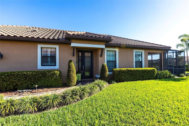 view of front of property featuring a front yard, glass enclosure, a tiled roof, and stucco siding