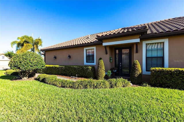 view of exterior entry with a lawn, a tile roof, and stucco siding