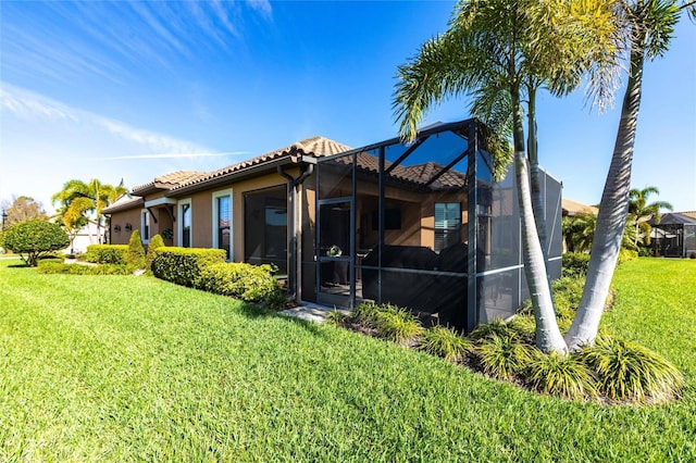 rear view of property with glass enclosure, a tiled roof, stucco siding, and a yard