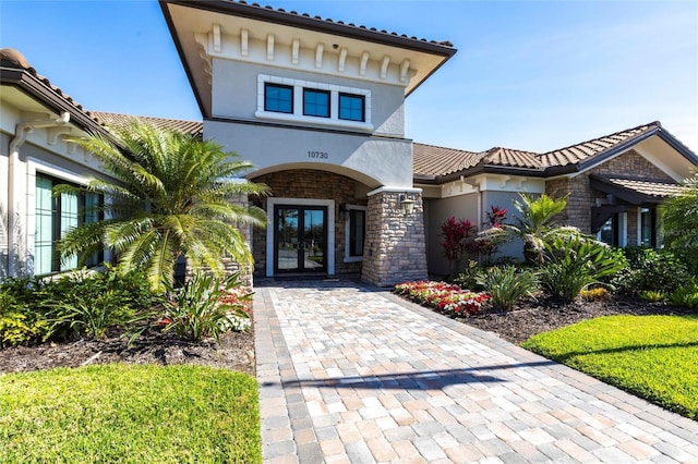 doorway to property featuring stone siding, french doors, a tile roof, and stucco siding