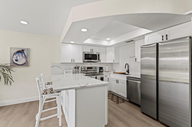 kitchen with light wood finished floors, appliances with stainless steel finishes, white cabinets, a sink, and a peninsula