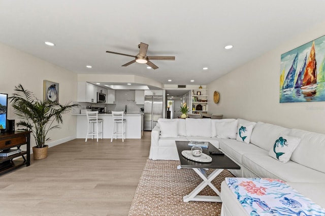 living room featuring a ceiling fan, recessed lighting, baseboards, and light wood finished floors