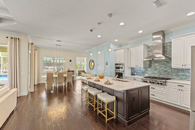 kitchen featuring stainless steel appliances, a sink, visible vents, wall chimney range hood, and decorative backsplash