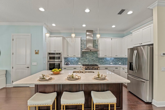 kitchen with dark wood-style flooring, white cabinetry, ornamental molding, appliances with stainless steel finishes, and wall chimney range hood