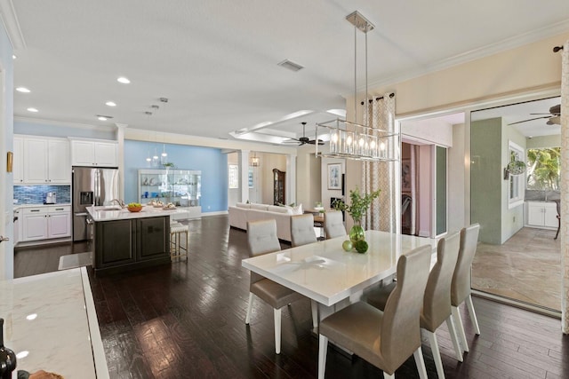 dining room with ceiling fan with notable chandelier, ornamental molding, dark wood finished floors, and visible vents