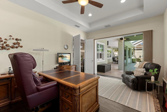 office with visible vents, a tray ceiling, and ceiling fan