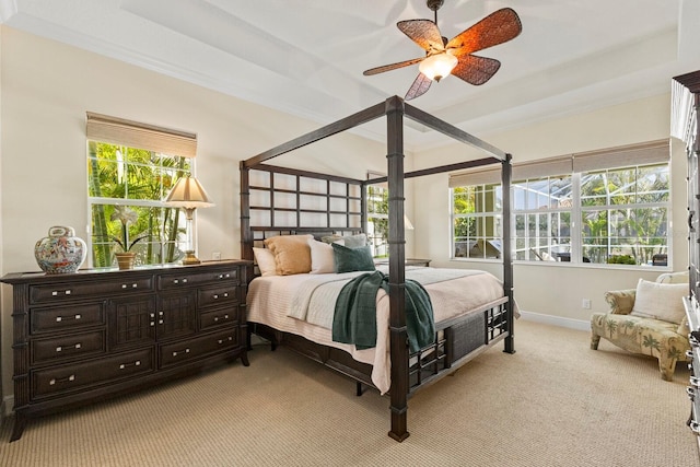 bedroom featuring light colored carpet, a ceiling fan, baseboards, a tray ceiling, and crown molding