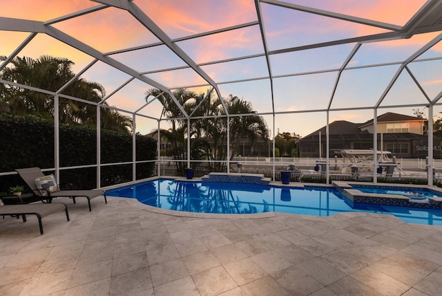 pool at dusk with a pool with connected hot tub, a patio area, and a lanai