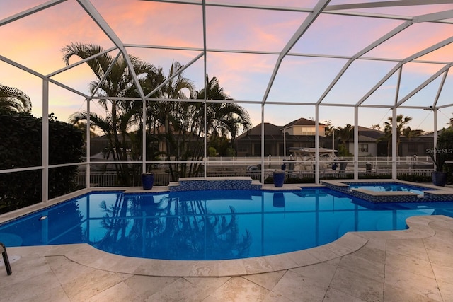 pool at dusk featuring a lanai, a patio area, and a pool with connected hot tub