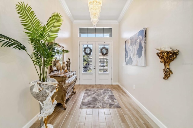 entrance foyer with light wood finished floors, baseboards, ornamental molding, an inviting chandelier, and french doors