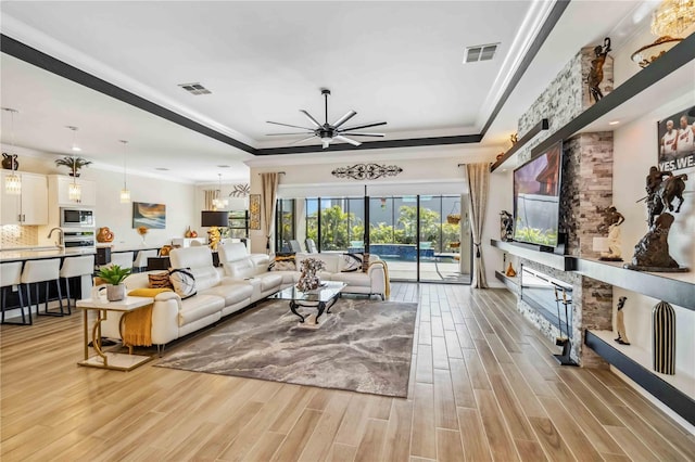 living area featuring light wood-type flooring, a raised ceiling, and visible vents