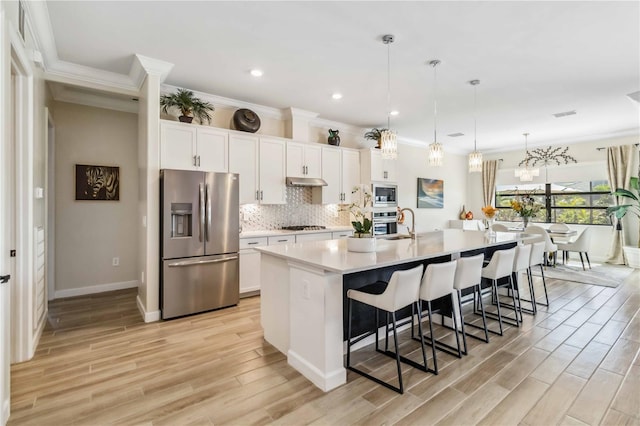 kitchen featuring under cabinet range hood, appliances with stainless steel finishes, a large island, light wood finished floors, and tasteful backsplash