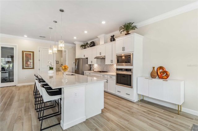 kitchen with a center island with sink, stainless steel appliances, decorative backsplash, under cabinet range hood, and a kitchen breakfast bar