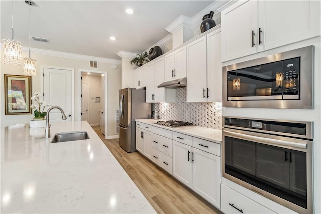 kitchen with under cabinet range hood, stainless steel appliances, white cabinetry, ornamental molding, and backsplash