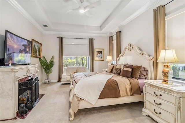 bedroom featuring a tray ceiling, crown molding, light colored carpet, visible vents, and a fireplace with flush hearth