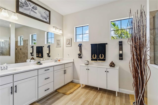 bathroom featuring wood finished floors, a sink, baseboards, double vanity, and walk in shower