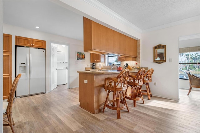 kitchen featuring a peninsula, light wood-style flooring, white fridge with ice dispenser, and brown cabinetry