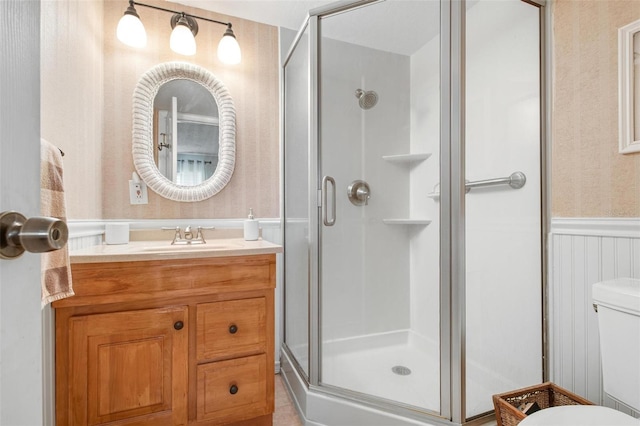 bathroom with toilet, wallpapered walls, a shower stall, and wainscoting