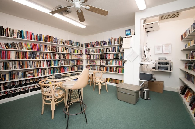 sitting room with ceiling fan, wall of books, carpet flooring, and visible vents